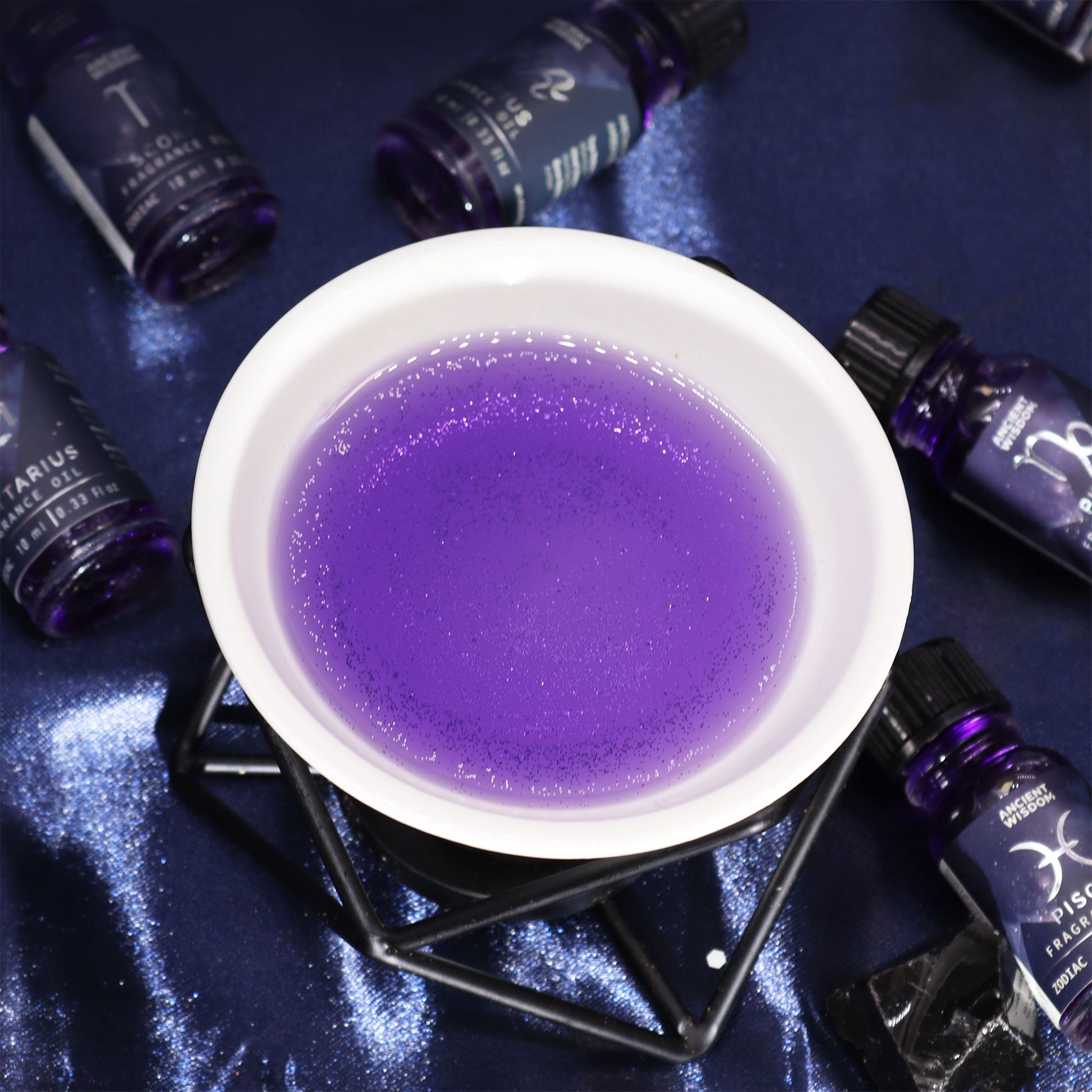 Violettes Duftöl mit Glitzer in einer Glasflasche, umgeben von weiteren Flaschen.