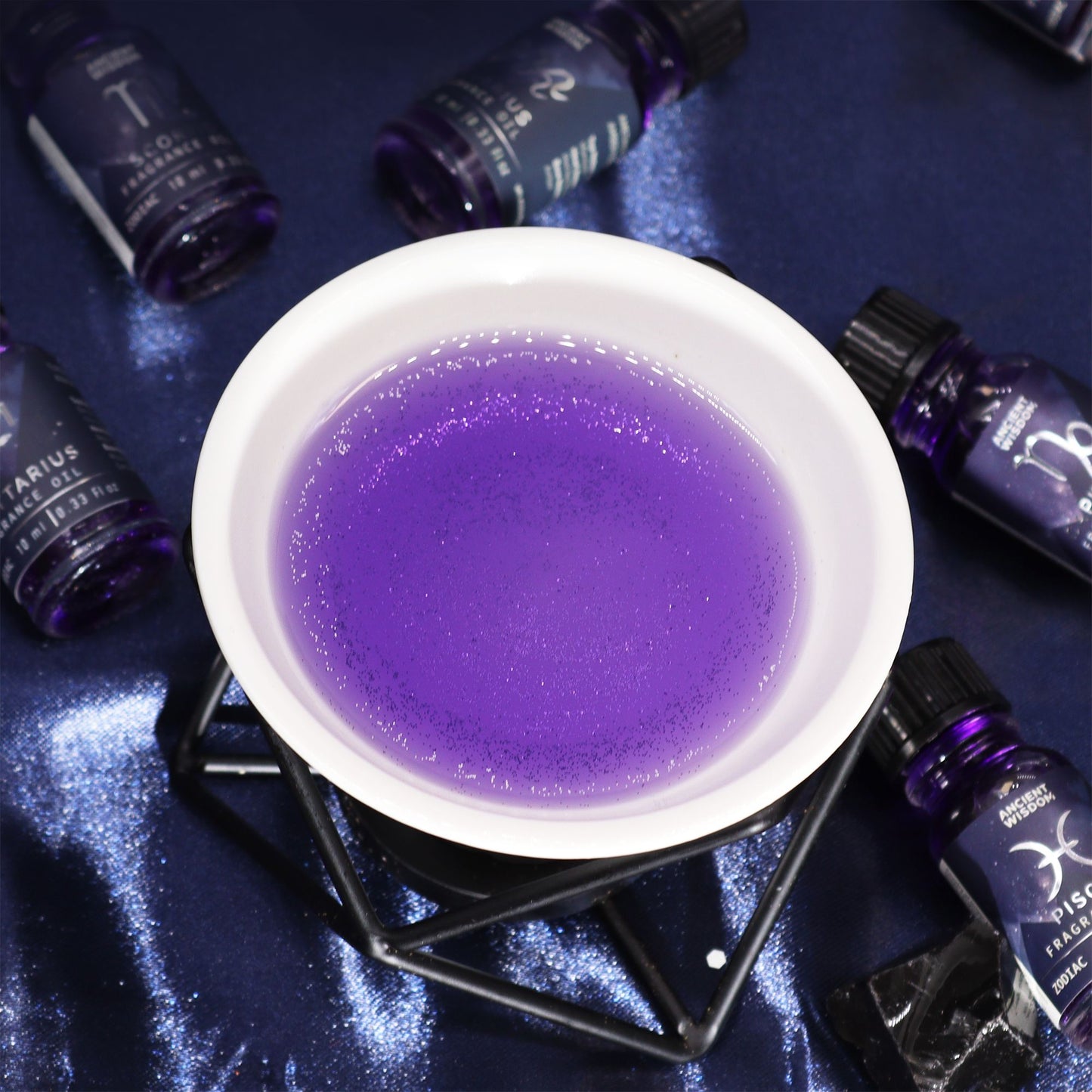 Violettes Duftöl mit Glitzer in einer Glasflasche auf blauem Untergrund.