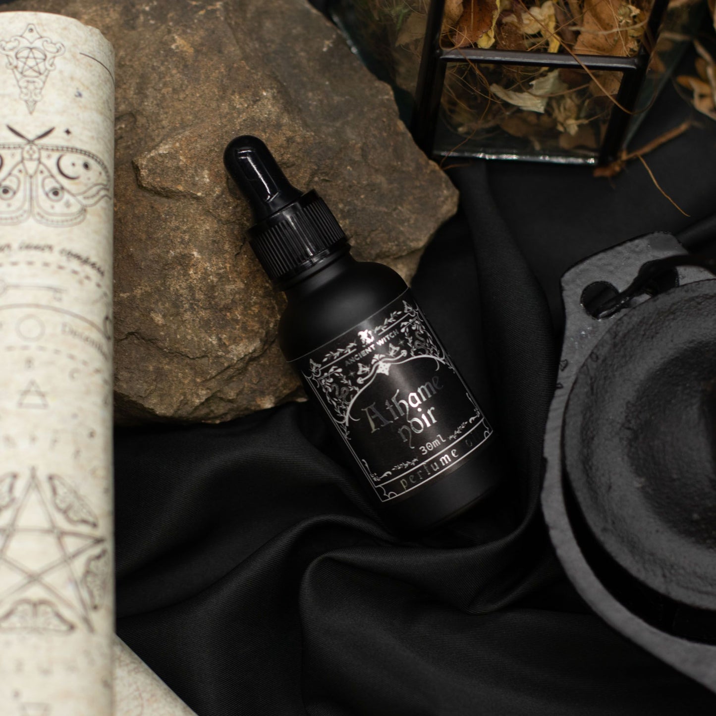 Black perfume oil bottle with Athame Noir label, on black fabric with rocks.