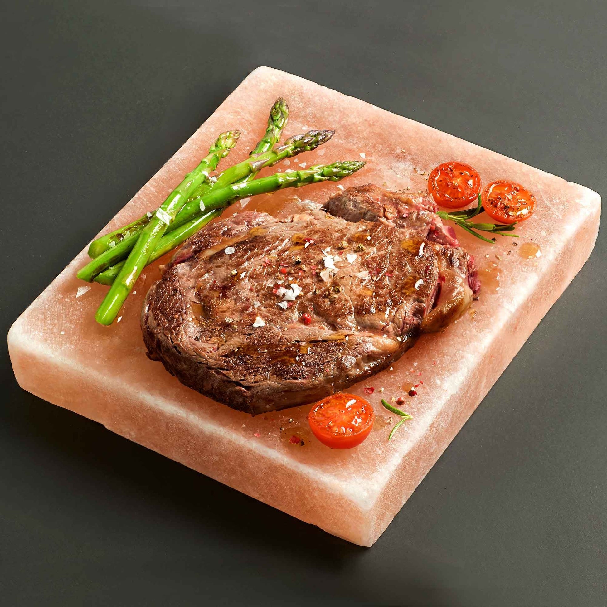 Quadratische Himalaya-Salzplatte mit Steak, Spargel und Tomaten.