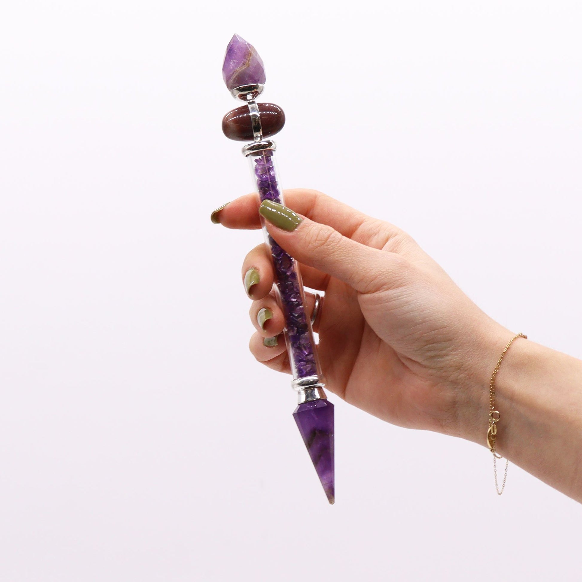 A hand holds a crystal wand with amethyst and a brown stone.