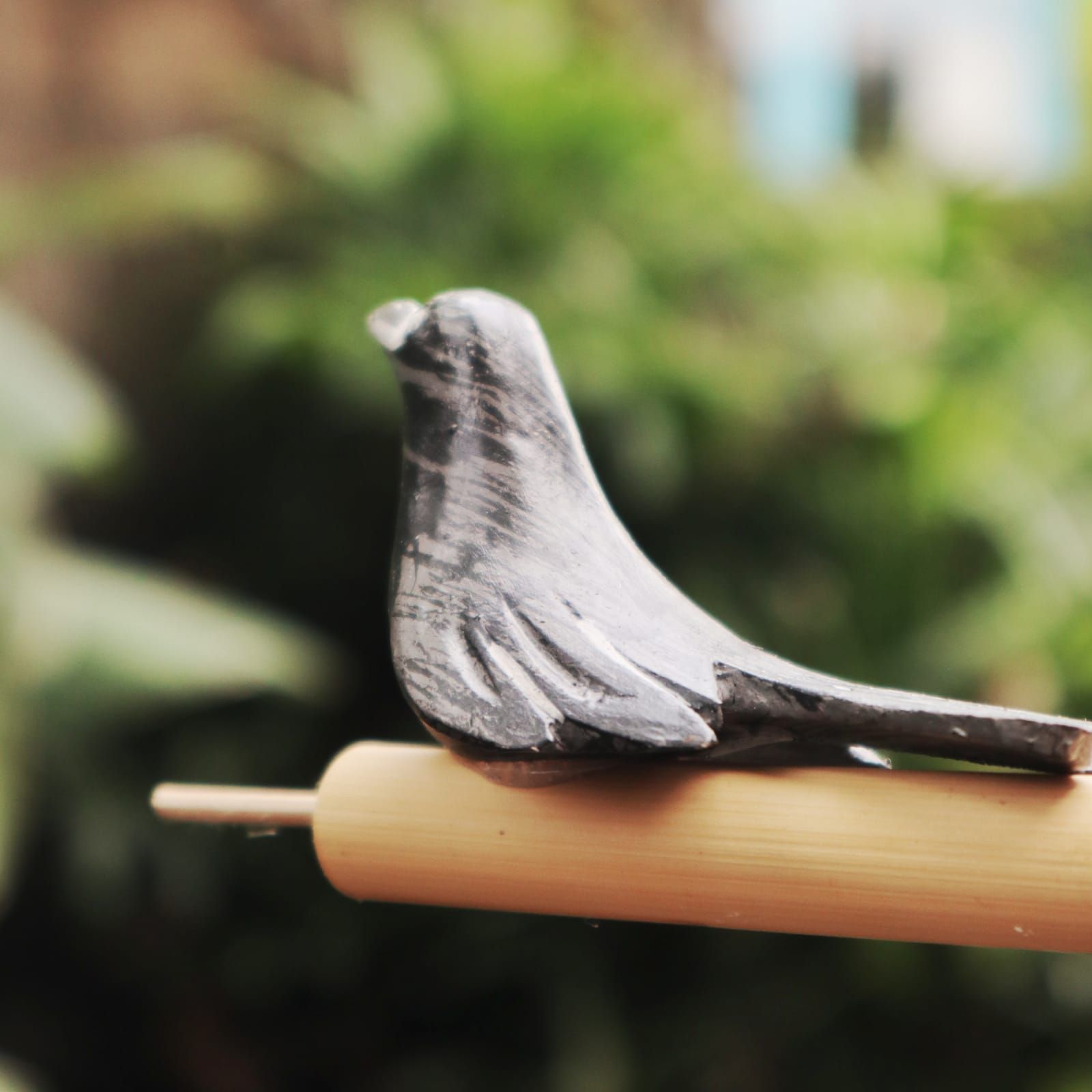 Wooden bird whistle with a gray, textured finish perched on a bamboo stick.