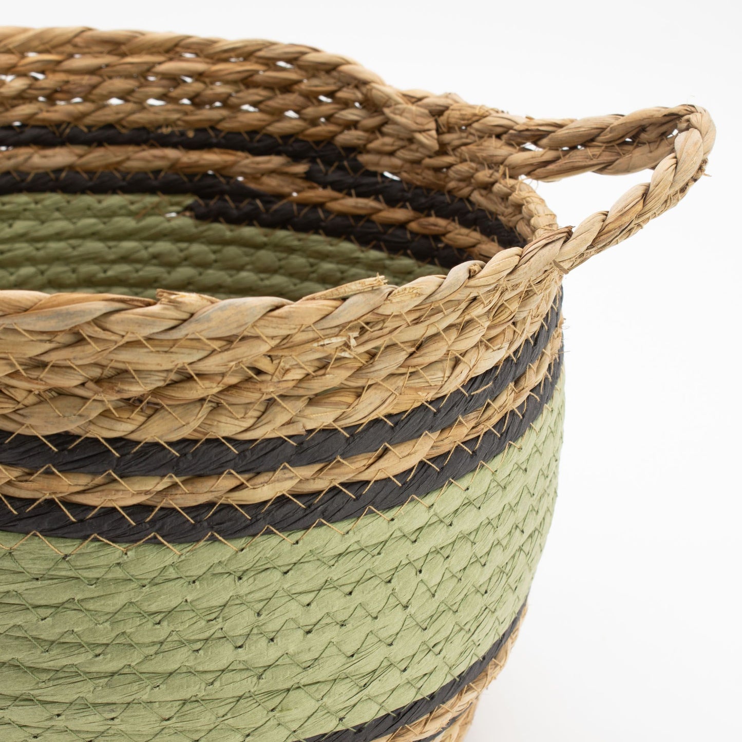A woven seagrass basket with natural, black, and green stripes and braided handles.