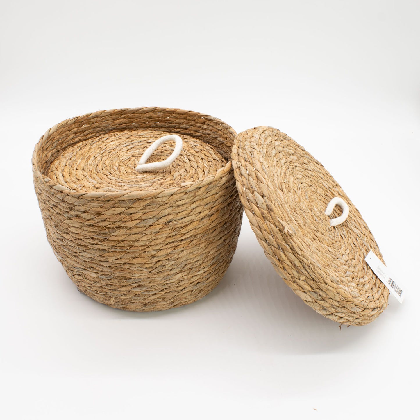 A round woven seagrass basket with a lid and a white rope handle.