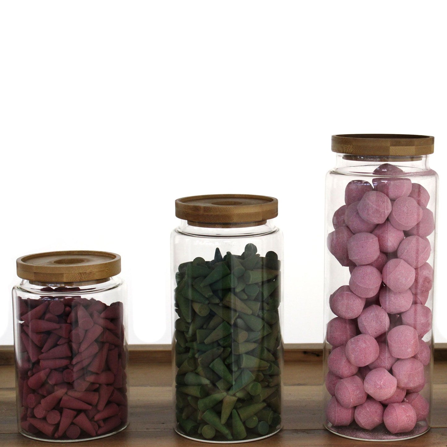 Vorratsglas aus Glas mit Bambusdeckel, gefüllt mit roten, grünen und rosa Konen.