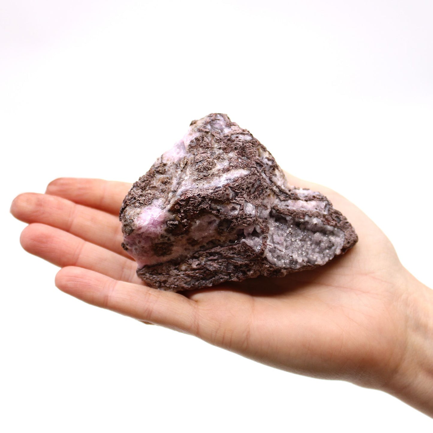 Ein roher Kobalt-Calcit-Stein in Rosa-Violett liegt in einer Hand.