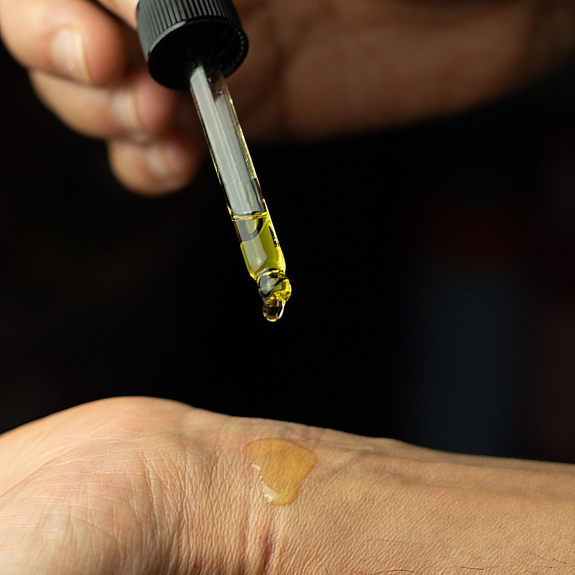 A dropper dispenses golden oil onto a person's wrist.