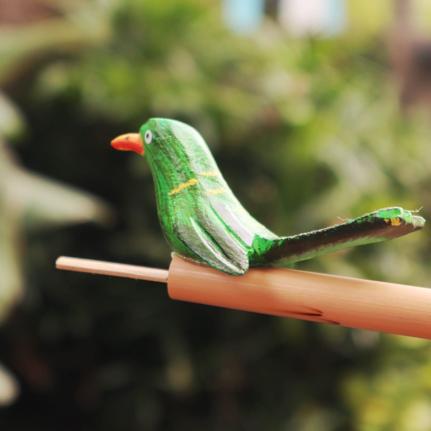 Green wooden bird whistle on a bamboo stick.