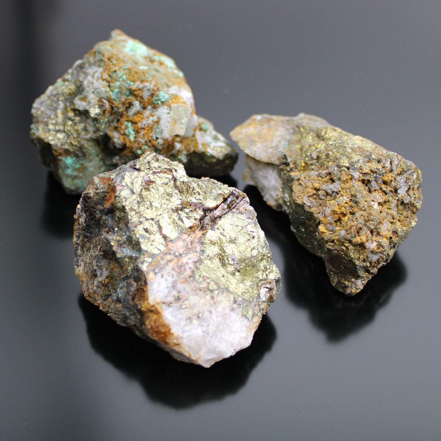 Drei rohe Chalkopyrit-Mineralien mit goldenem Glanz und türkisfarbenen Einschlüssen.