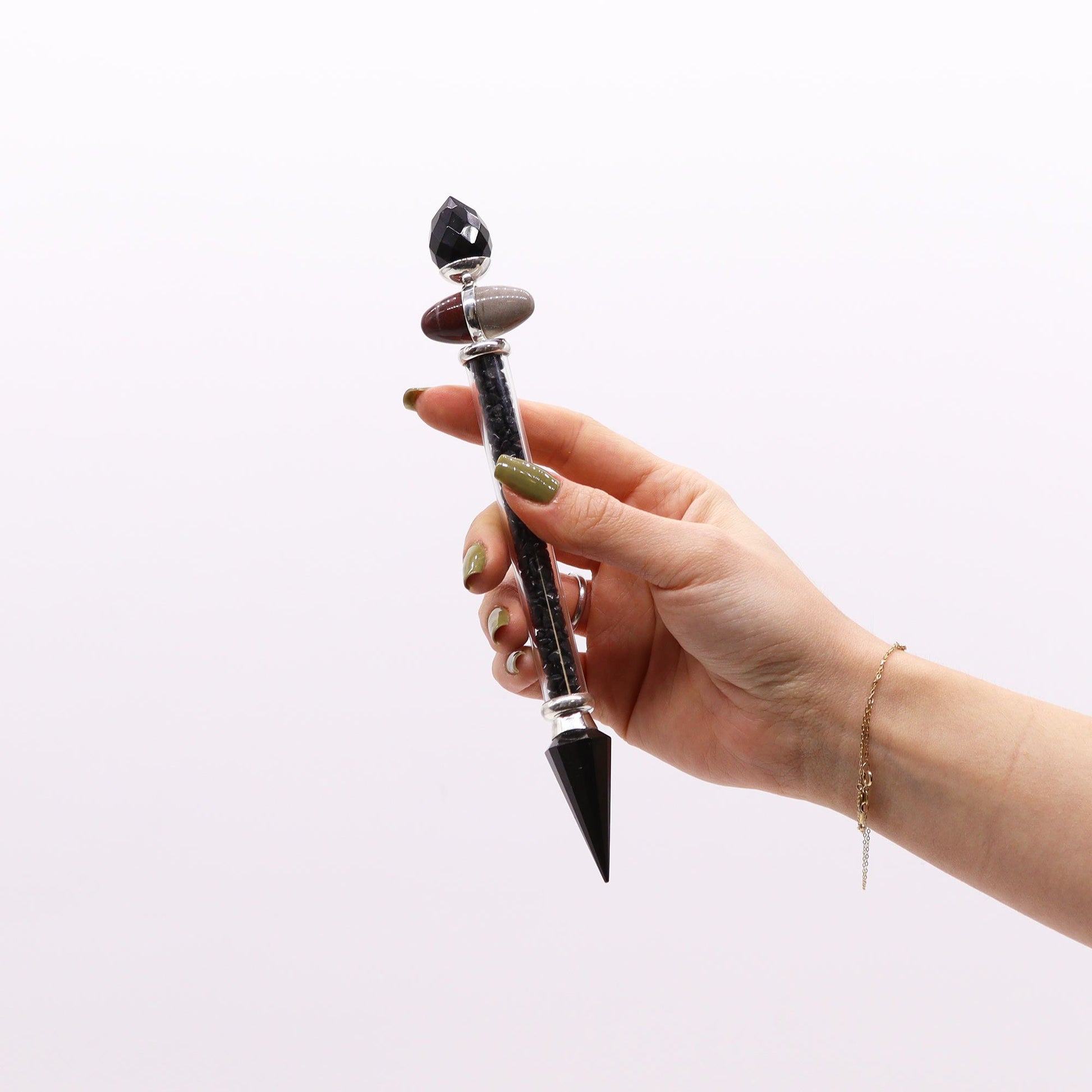 A hand holds a black tourmaline and agate Shiva Lingam magic wand.
