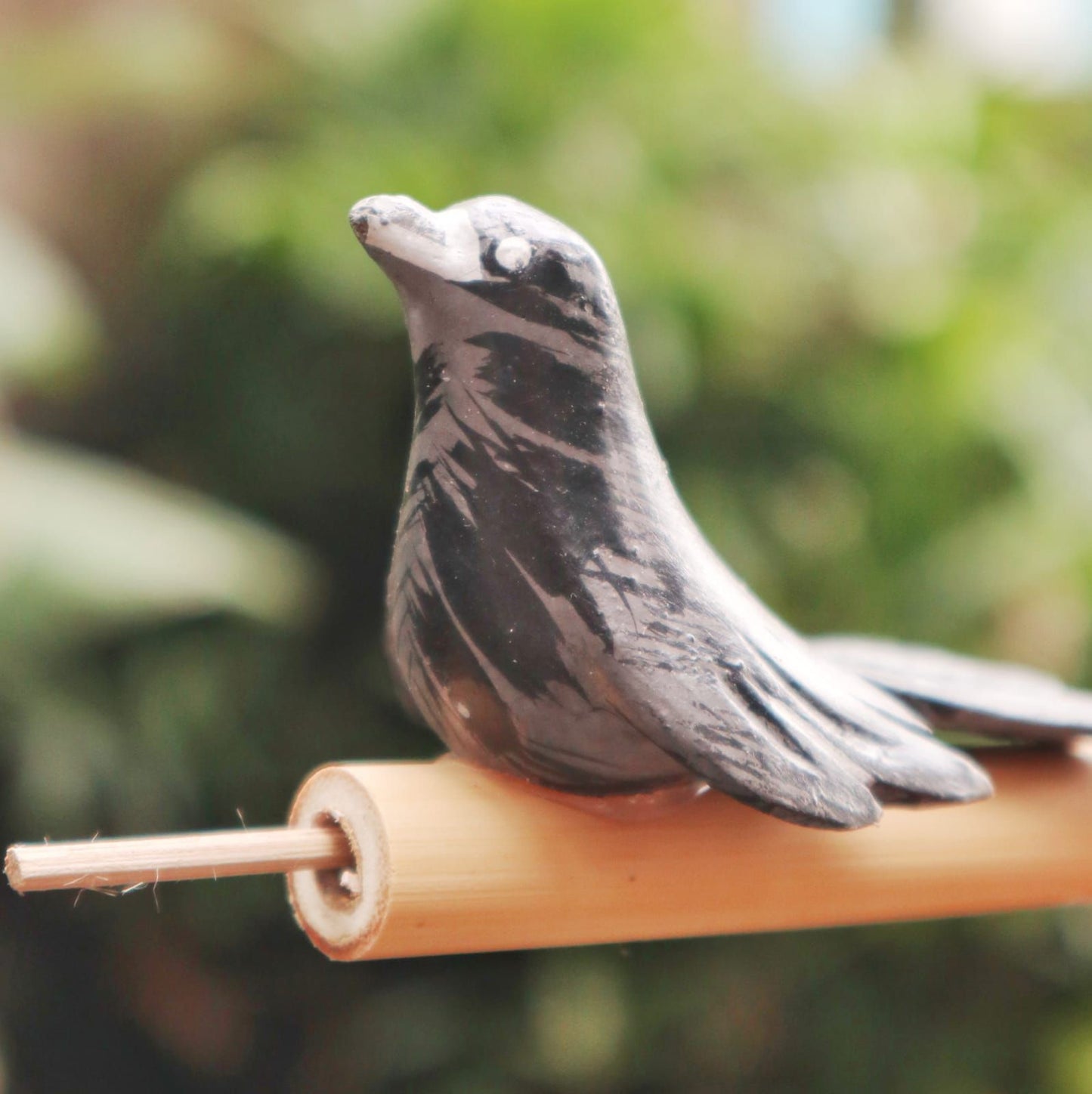 A small, dark gray ceramic bird figurine with white accents sits on a bamboo perch.
