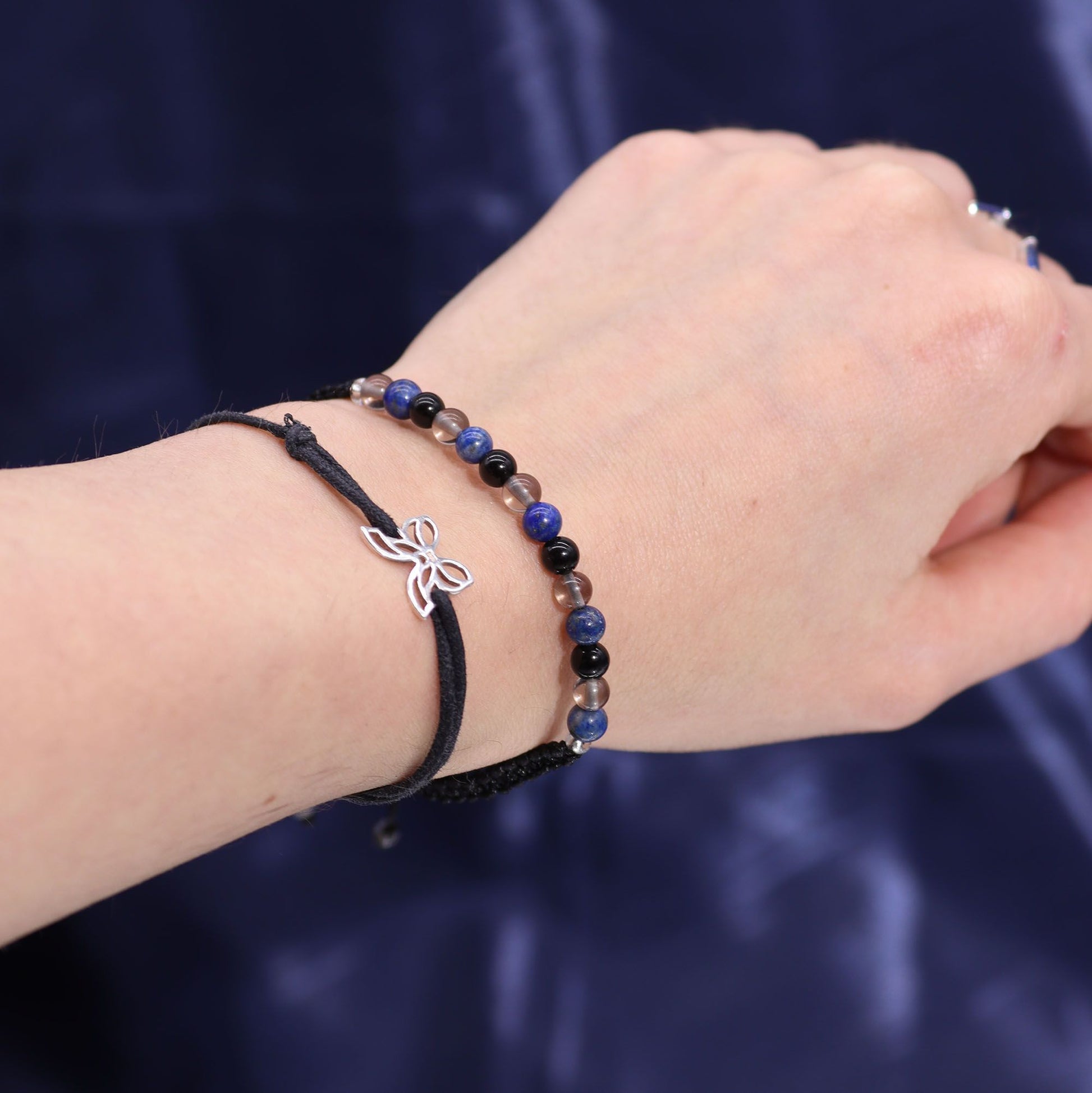 Ein Armband mit blauen und schwarzen Perlen und einem Schmetterlingsanhänger.