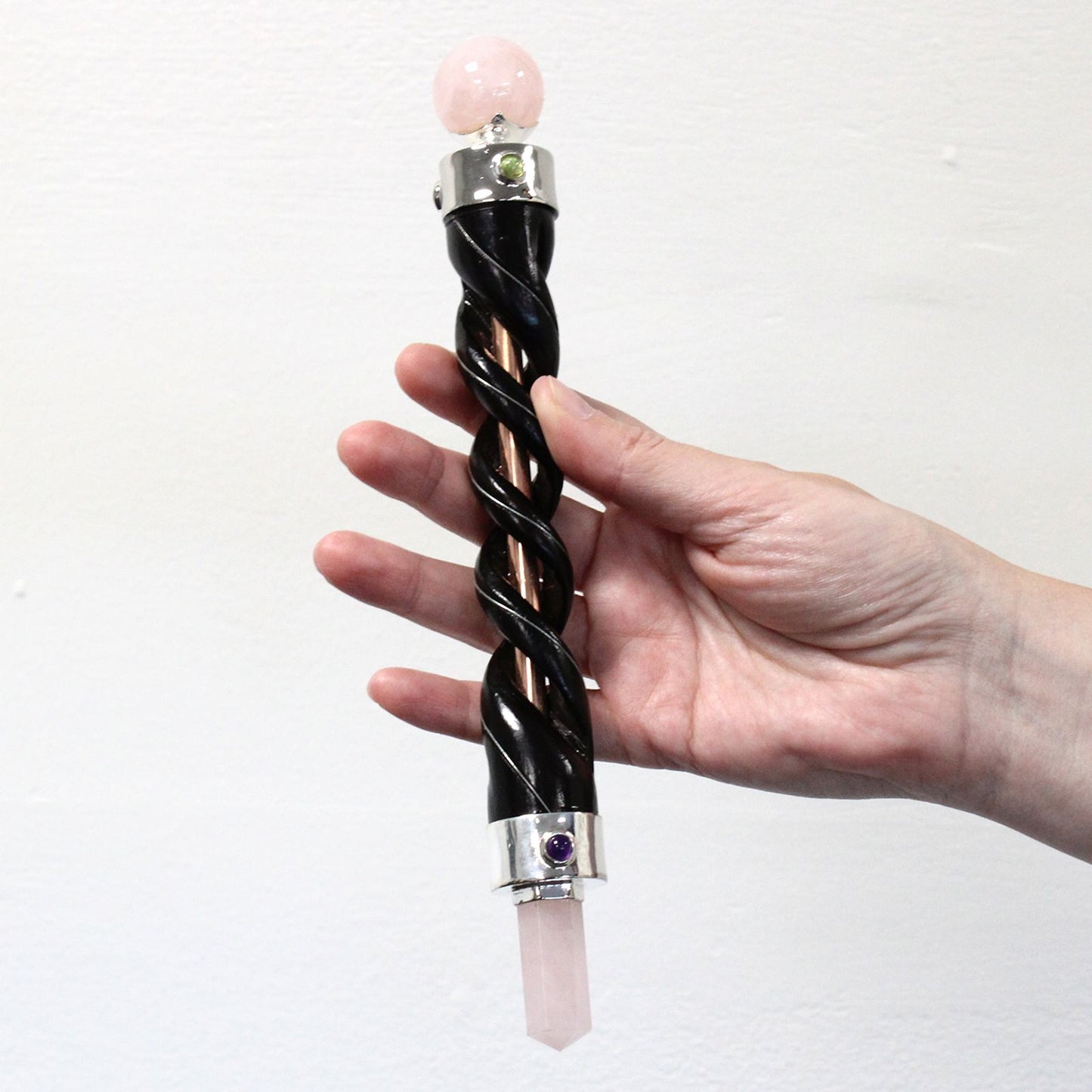 A hand holds a spiral carving healing wand with copper pipe and rock quartz.