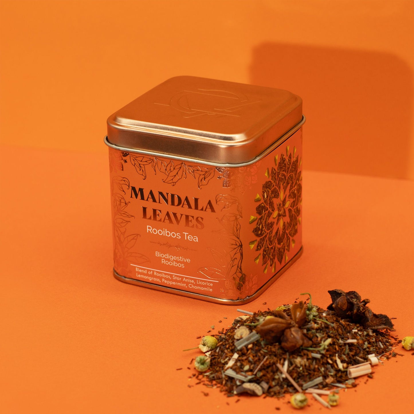 A copper tin of Mandala Leaves Rooibos Tea with a pile of loose tea leaves.