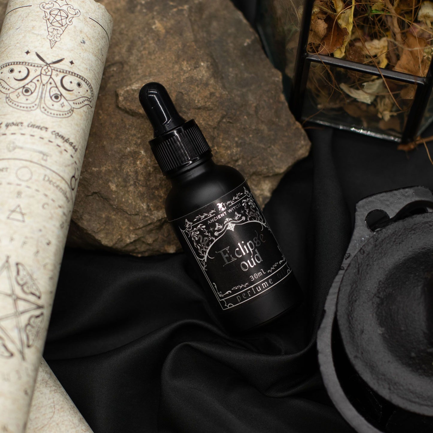 Black bottle of Eclipse Oud perfume oil with a dropper, on a dark fabric.