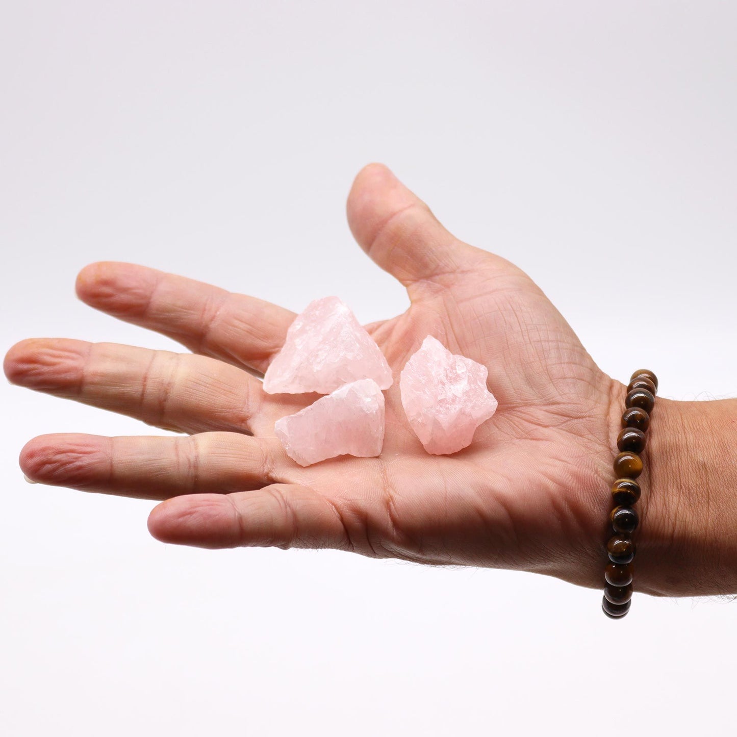 Hand holding rough pink rose quartz stones with a tiger's eye bracelet.