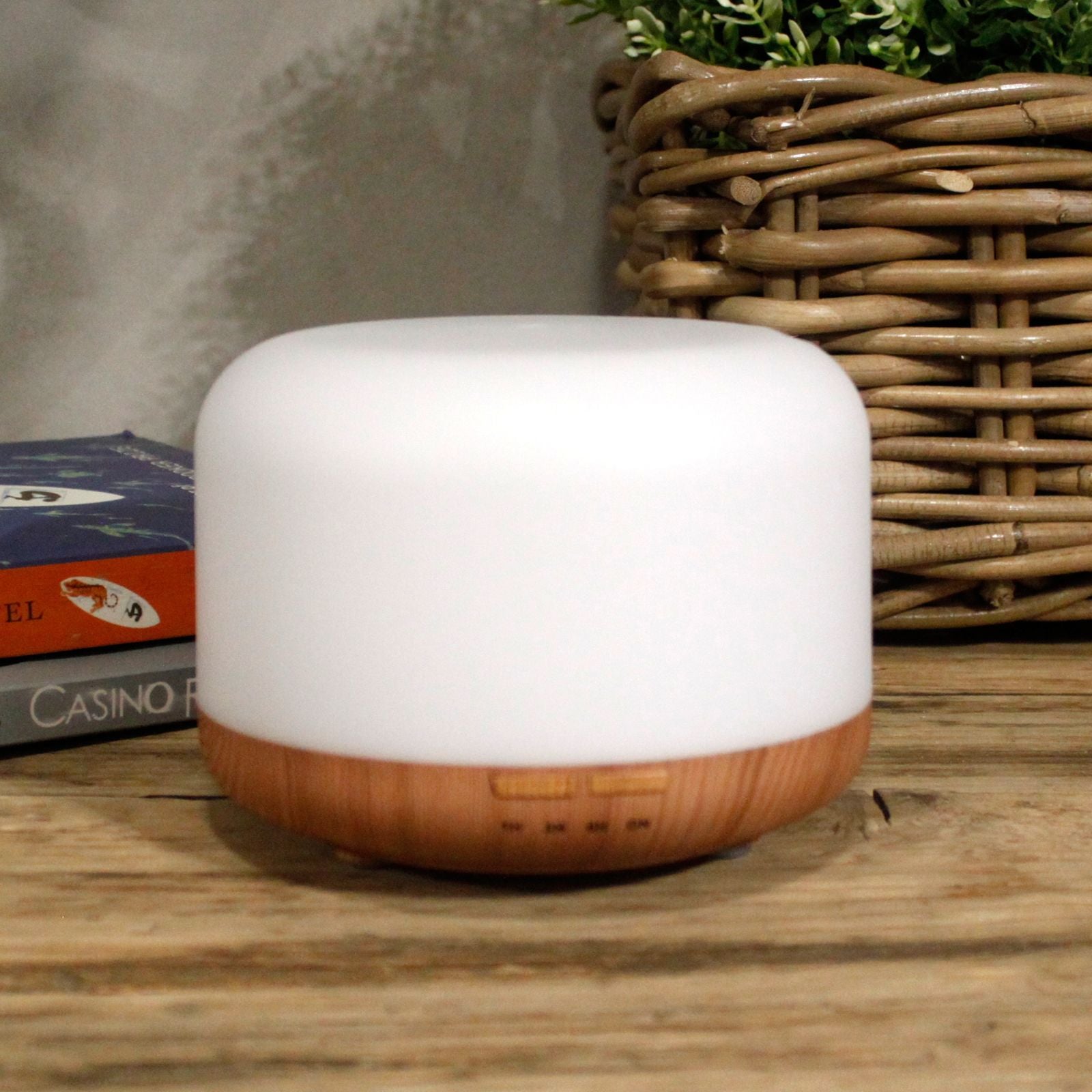 A white and wood-grain aroma diffuser with a woven basket and books in the background.