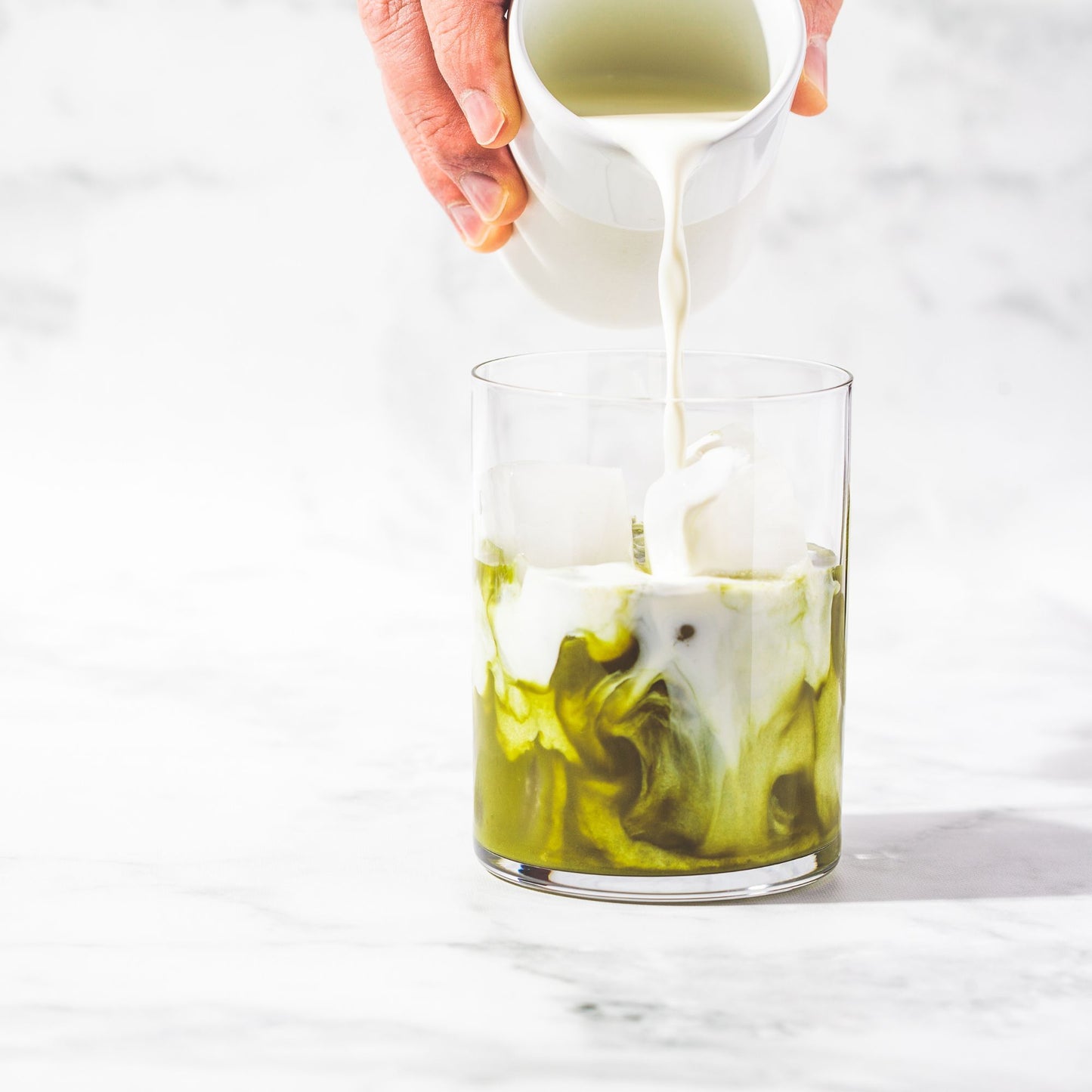 Cream being poured into a glass of iced matcha tea.