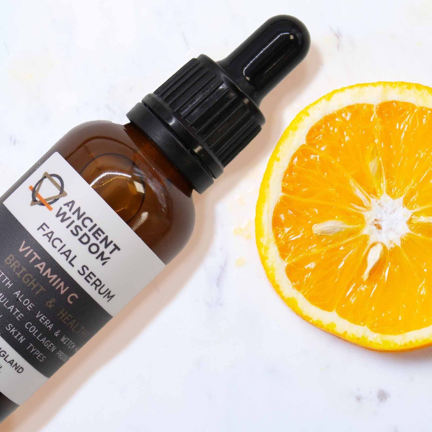 Vitamin C Gesichtsserum mit Aloe Vera und Zaubernuss in einer Braunglasflasche neben einer Orangenscheibe.