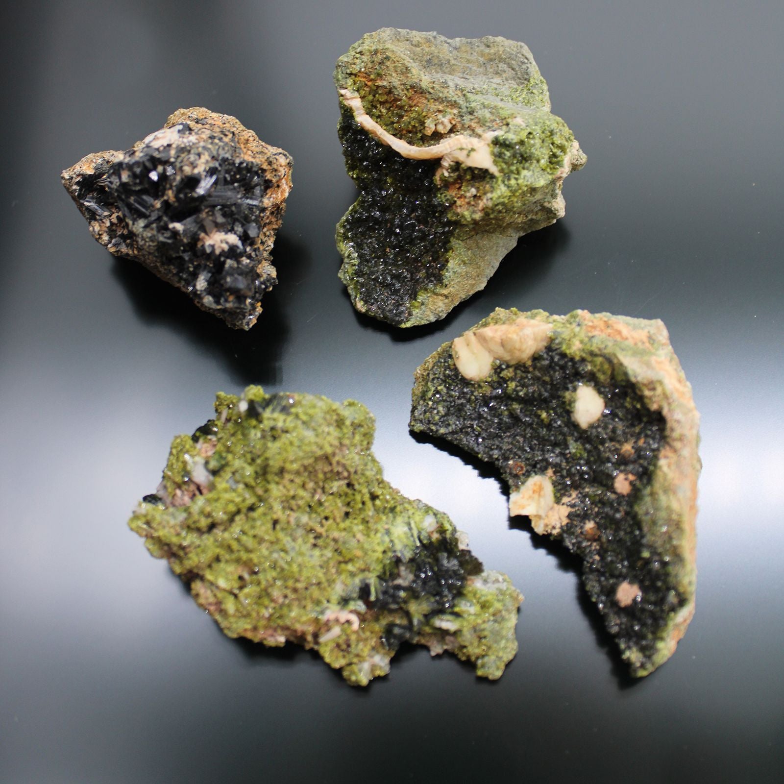 Vier rohe Epidot-Kristall-Stücke mit dunklen und hellgrünen Mineralien.