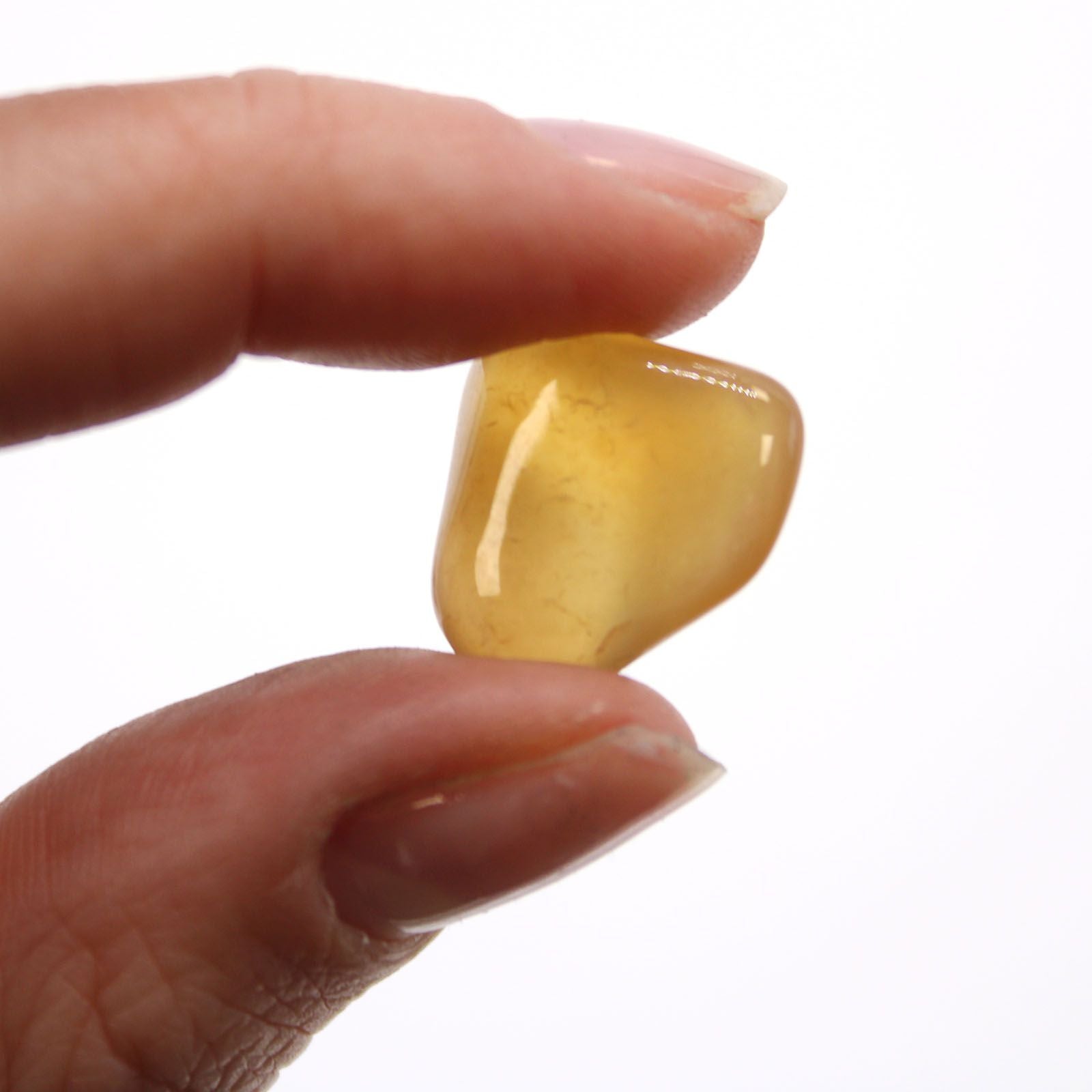 Zwei Finger halten einen kleinen, glatten, gelben Trommelstein.