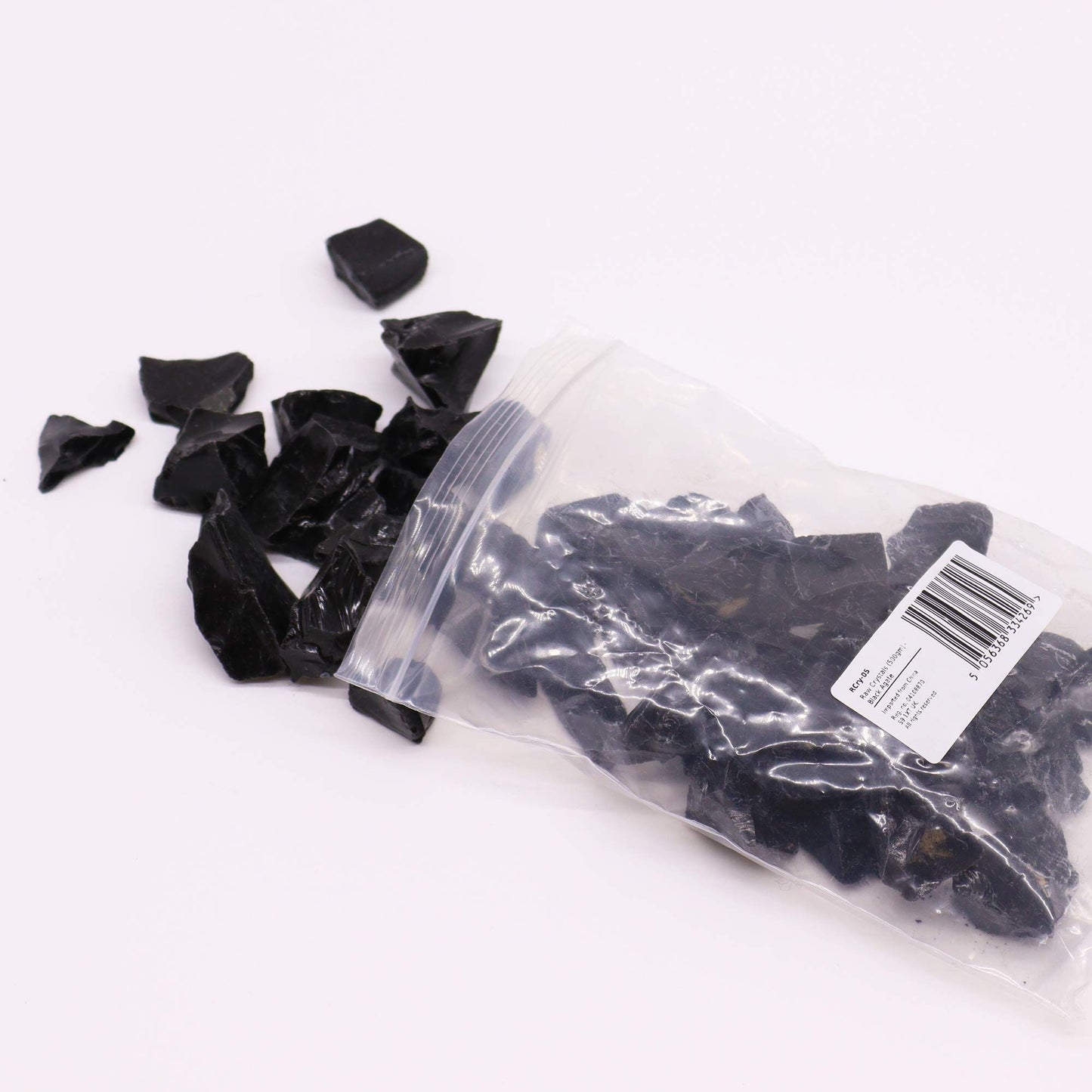 Schwarze Obsidian-Rohsteine in einer Plastiktüte und lose verstreut.
