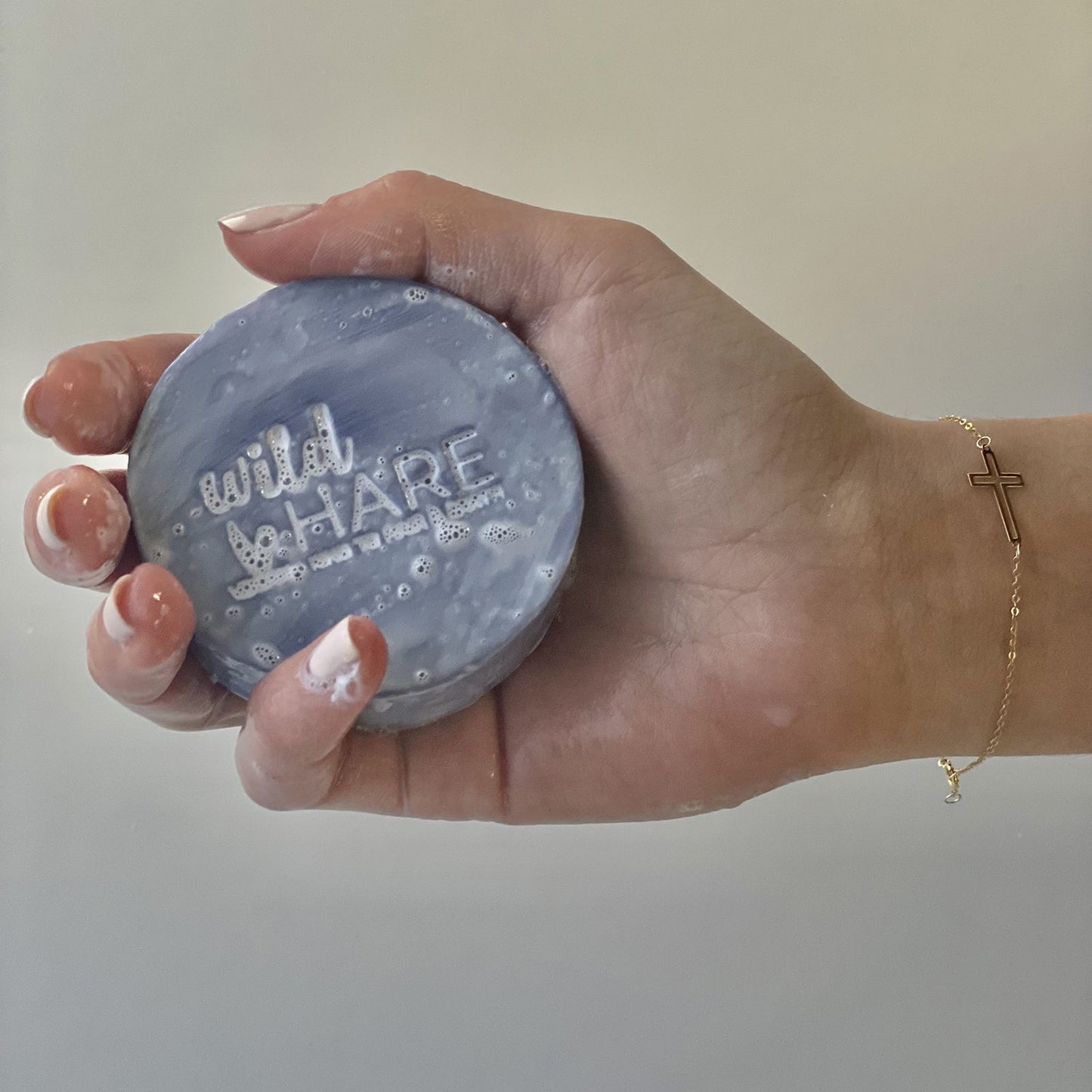 A hand holds a round, blue solid shampoo bar with "Wild Hare" embossed on it.
