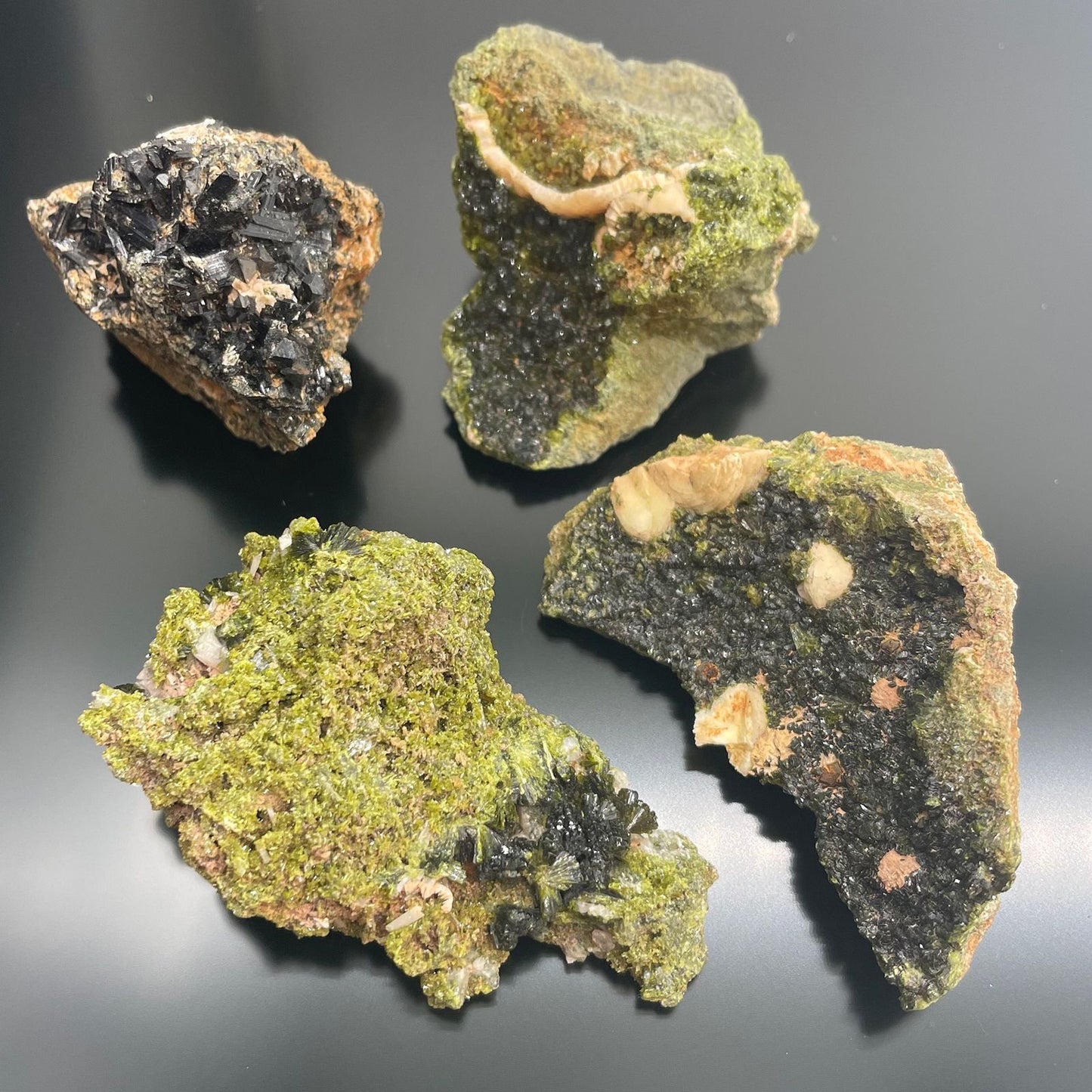 Vier rohe Epidot-Kristallbrocken mit grünen und schwarzen Mineralien.