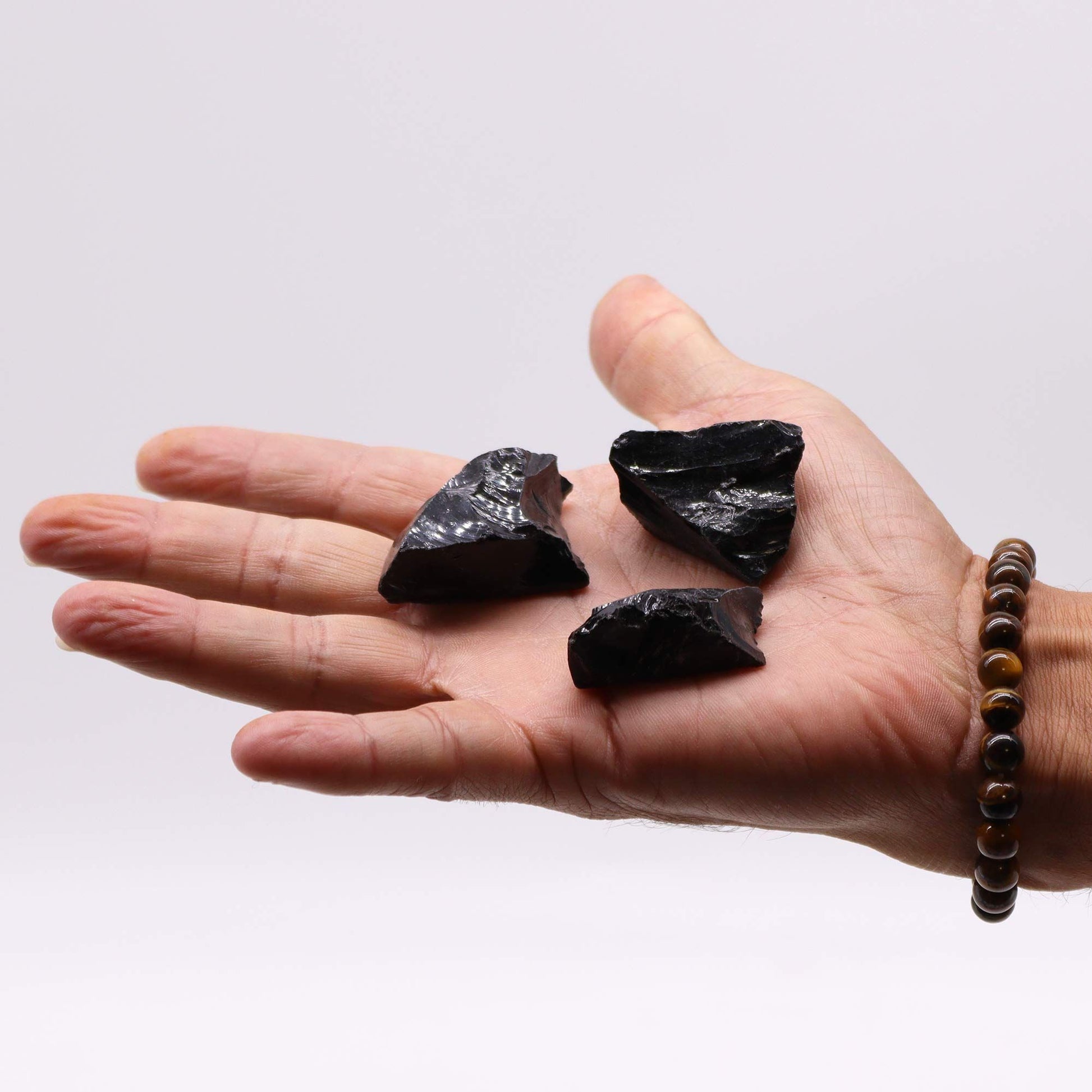 Drei rohe schwarze Obsidiansteine liegen in einer Hand.