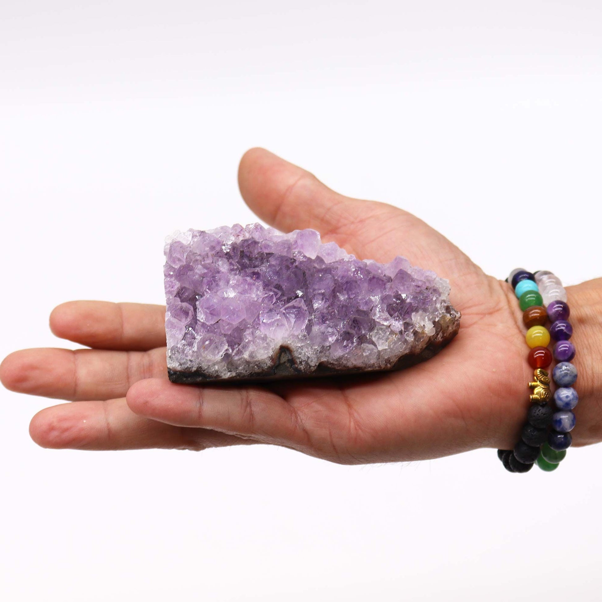 Eine Hand hält einen natürlichen Amethyst-Cluster mit violetten Kristallen.