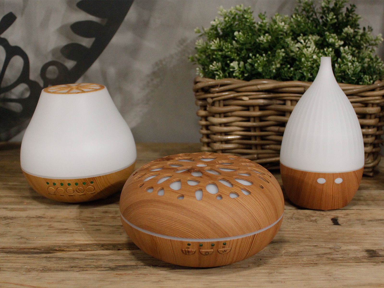 Three aroma diffusers with wood-grain bases and white tops sit on a wooden surface.
