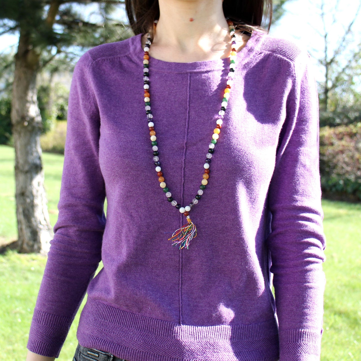 A woman wears a purple sweater with a colorful beaded mala necklace.