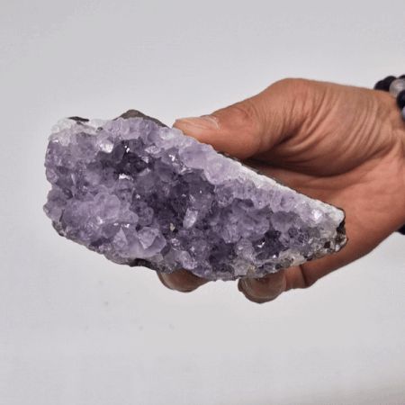 Eine Hand hält einen mittelgroßen, natürlichen Amethyst-Cluster mit violetten Kristallen.