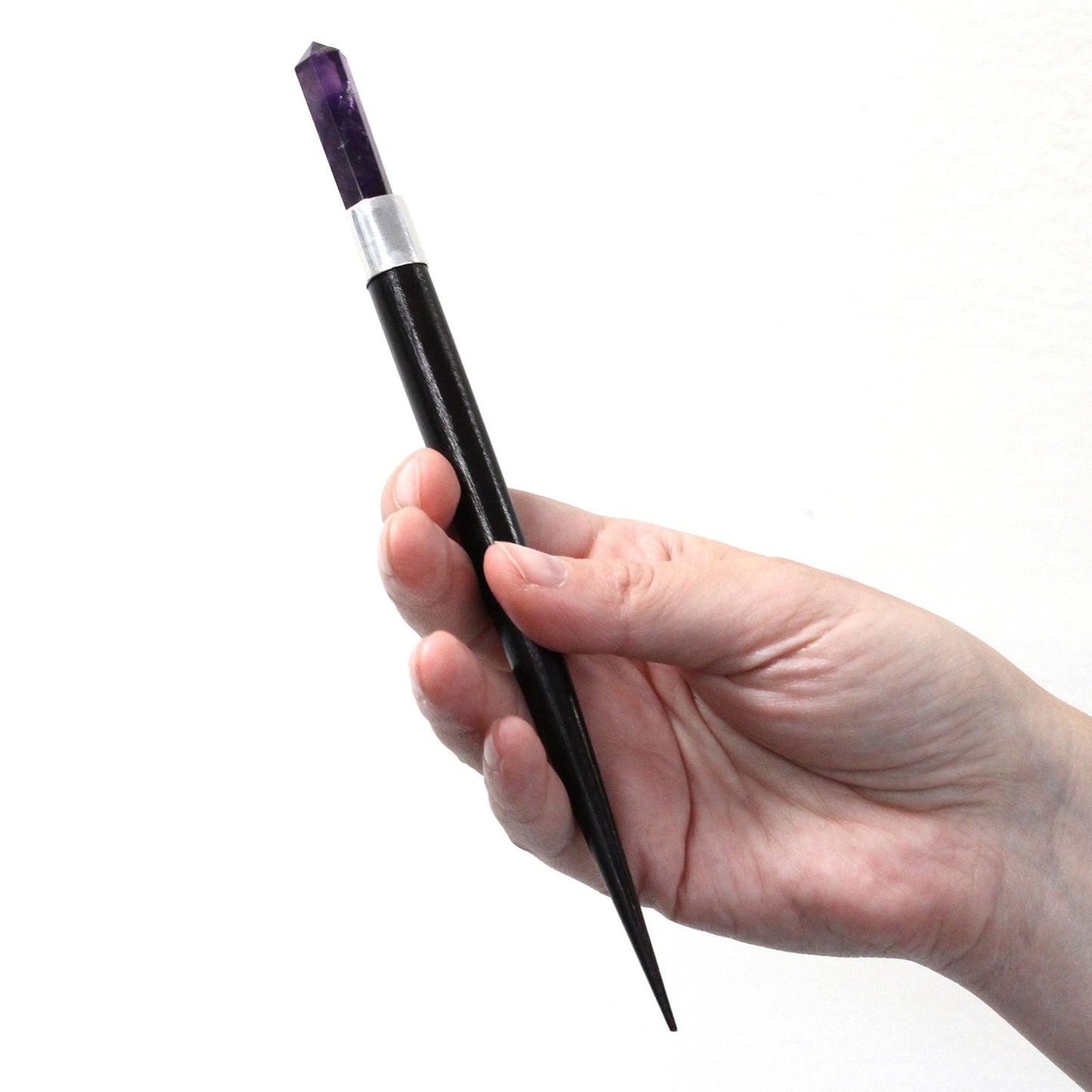 Hand holding a black wand with a pointed amethyst crystal tip.