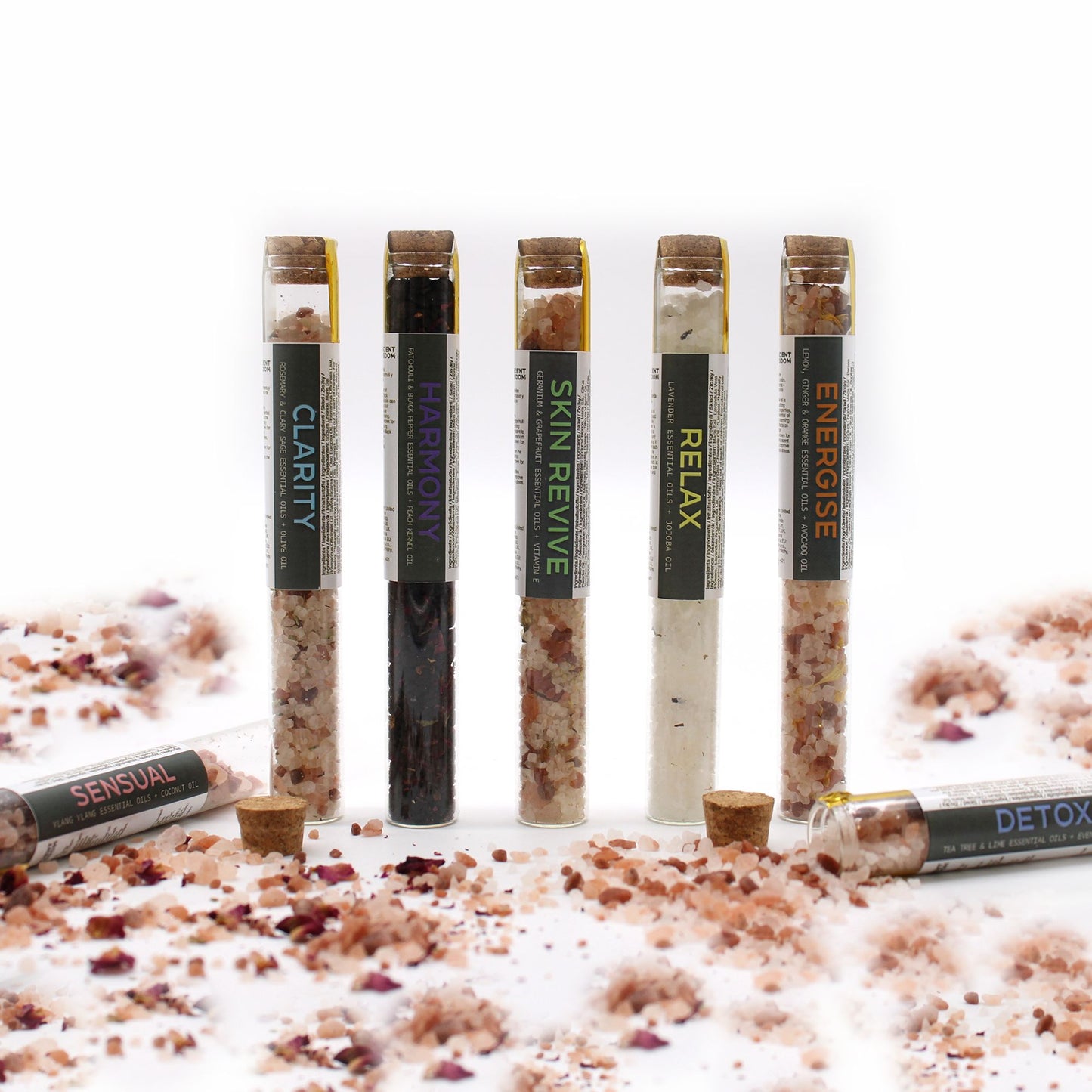 Seven vials of bath salts with cork stoppers and labels, scattered with bath salts and rose petals.