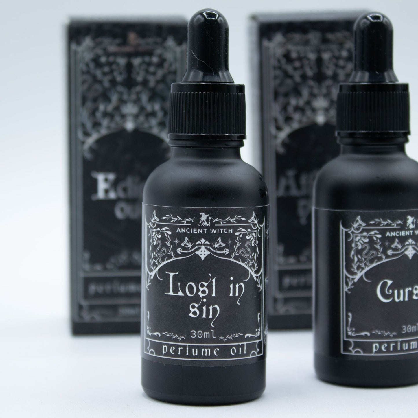 Two black perfume oil bottles with ornate labels, one reading "Lost in Sin".