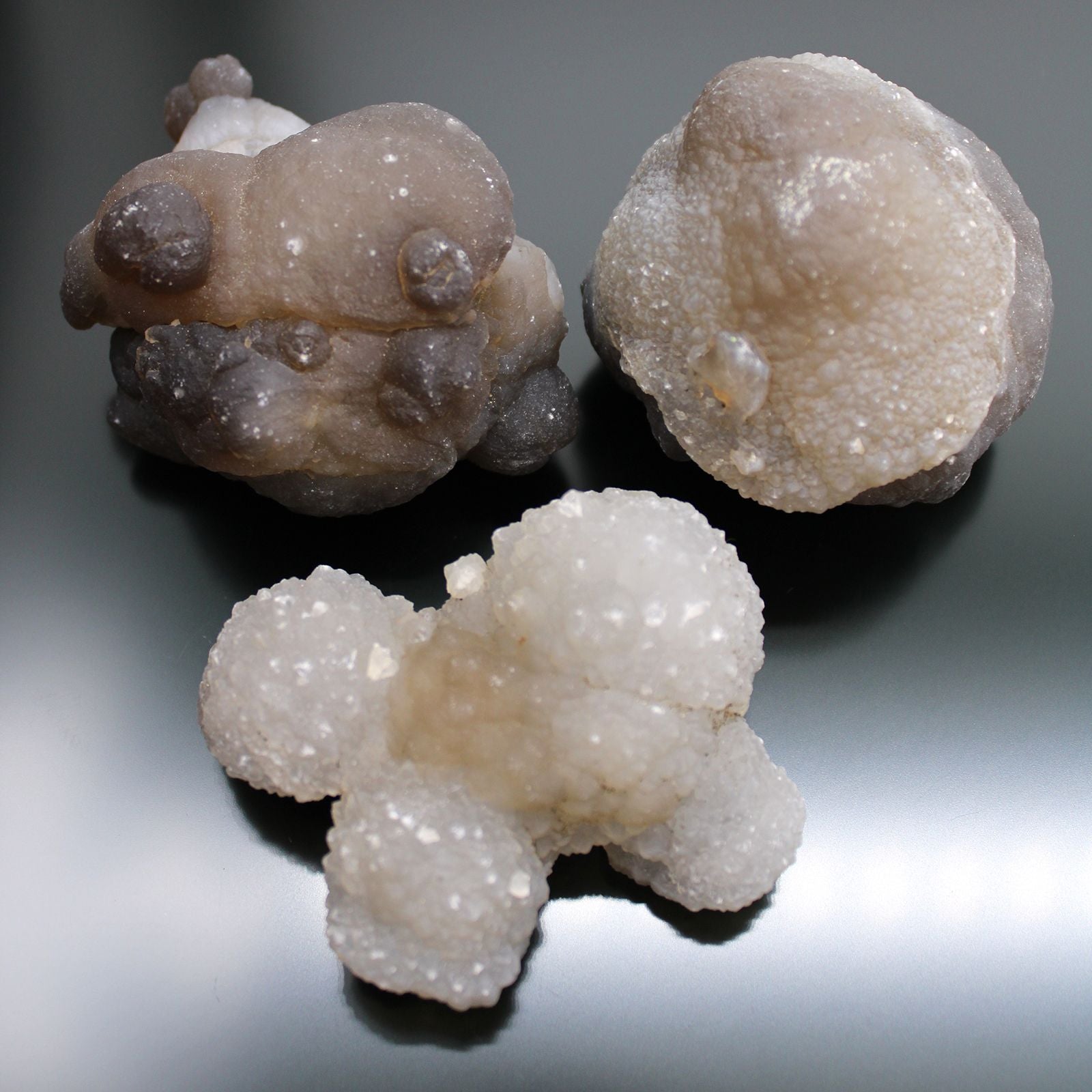 Drei rohe Chalcedon-Kristalle in verschiedenen Grautönen und Weiß.