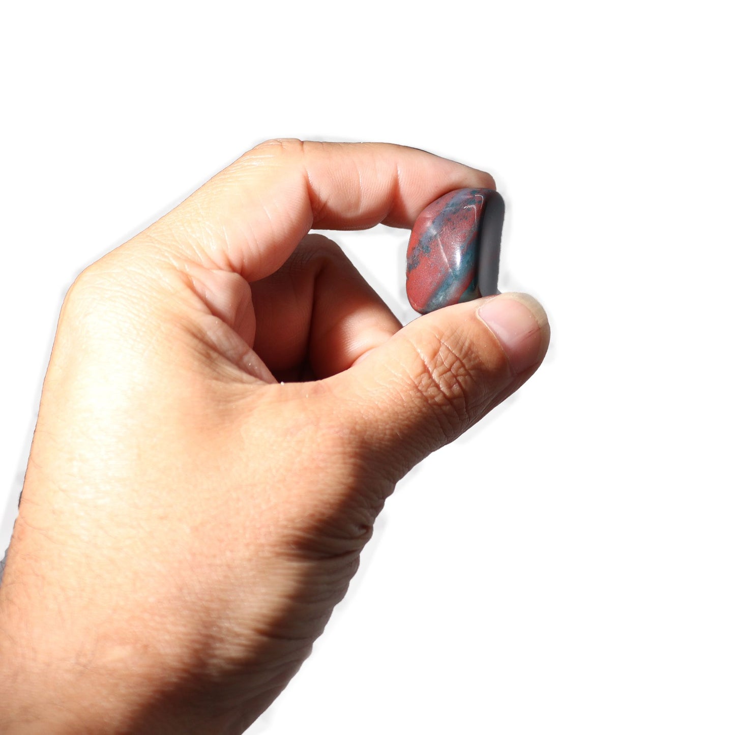 Hand holding a tumbled bloodstone with red and blue-green markings.
