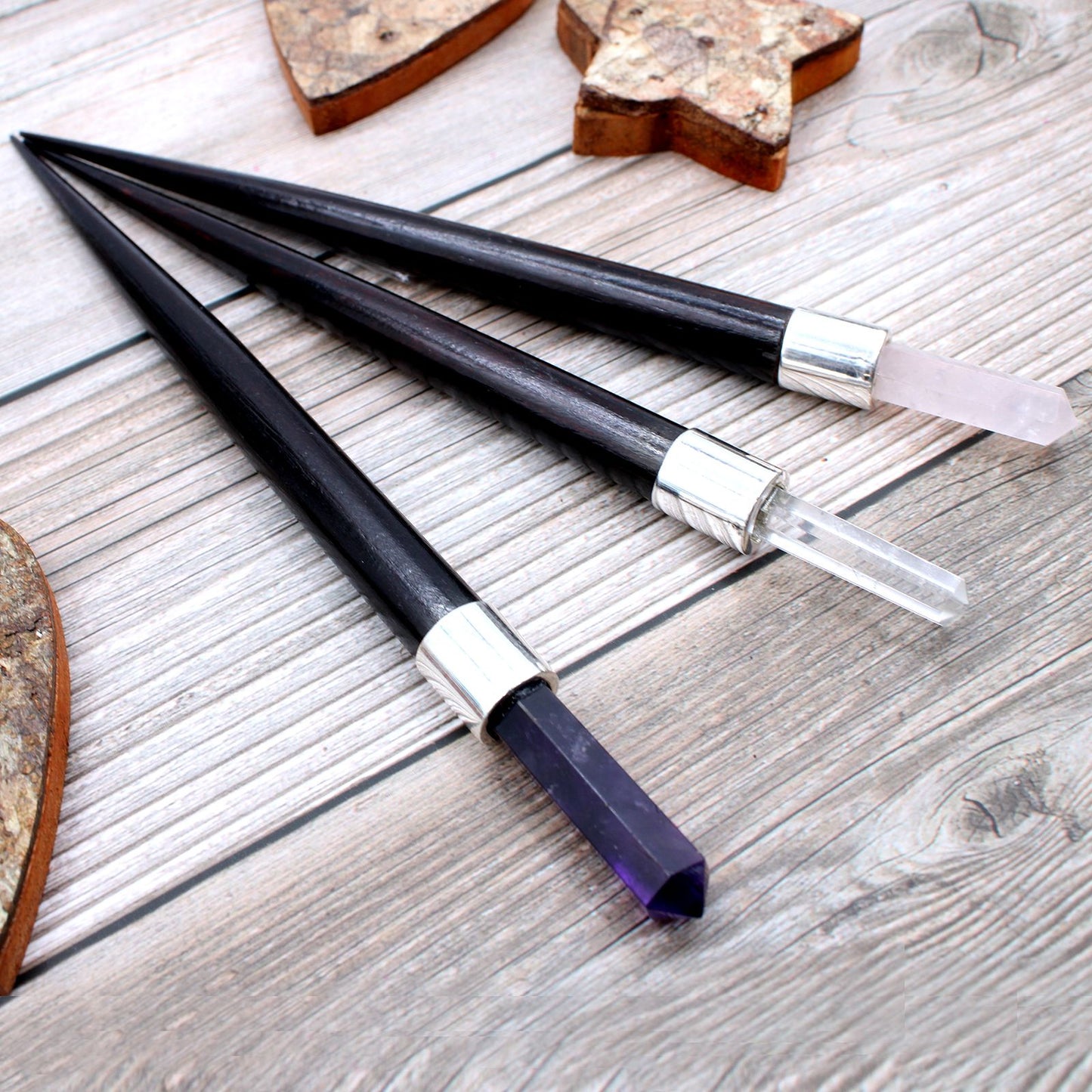 Three pointed healing wands with dark handles and crystal tips in rose, clear, and amethyst.