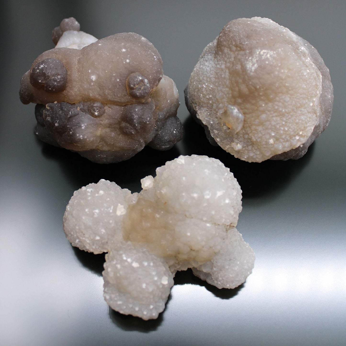Drei rohe Chalcedon-Kristalle in verschiedenen Grautönen und Weiß.