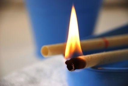 Two lavender-scented ear candles, one lit, with a flame.