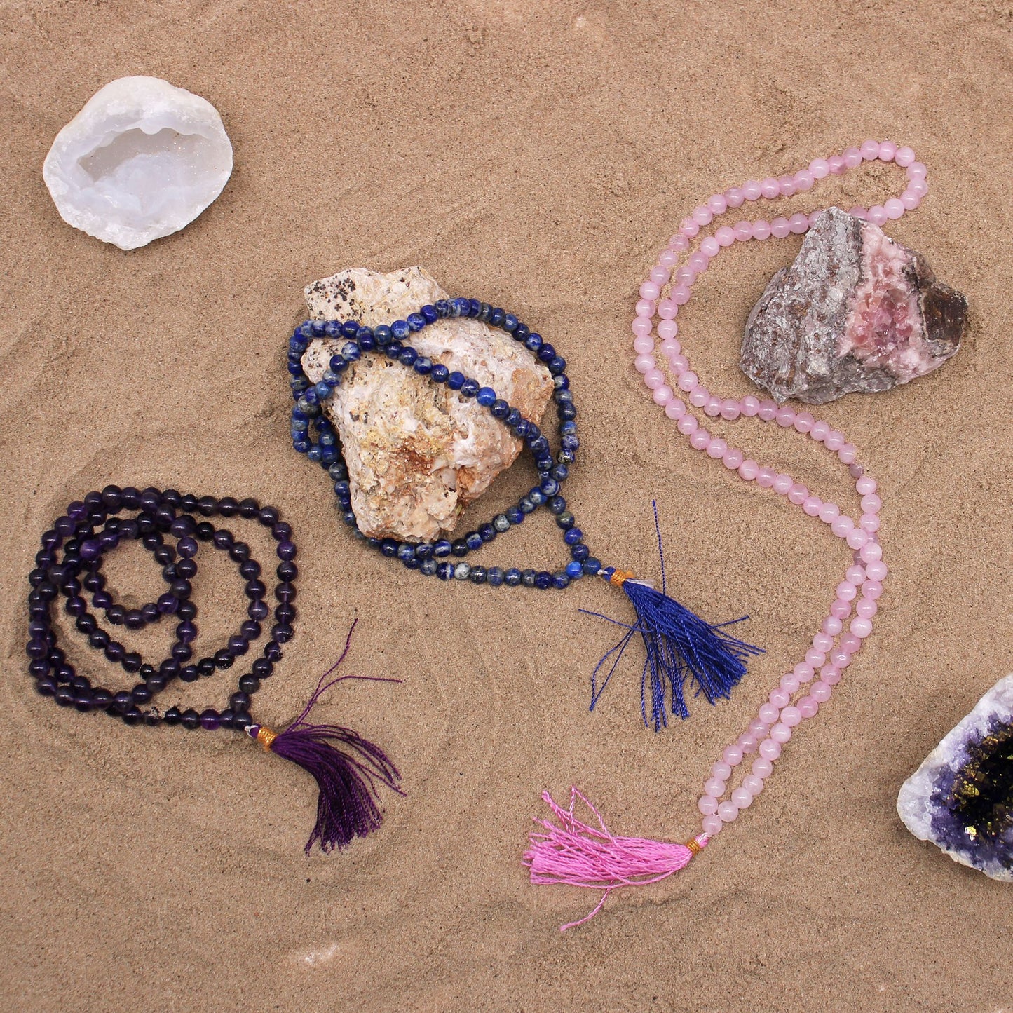 Amethyst mala with a purple tassel on sand.