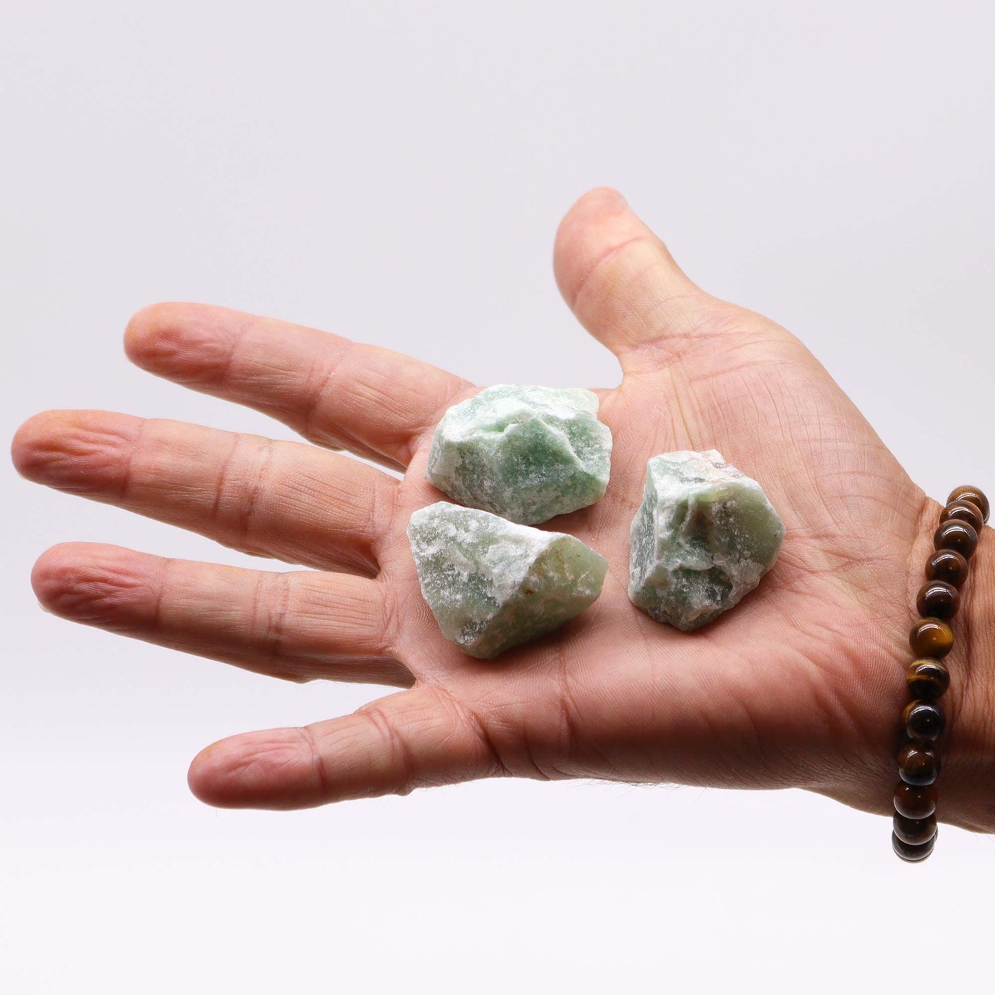 Drei rohe Jadeit-Rohsteine liegen in einer Hand.