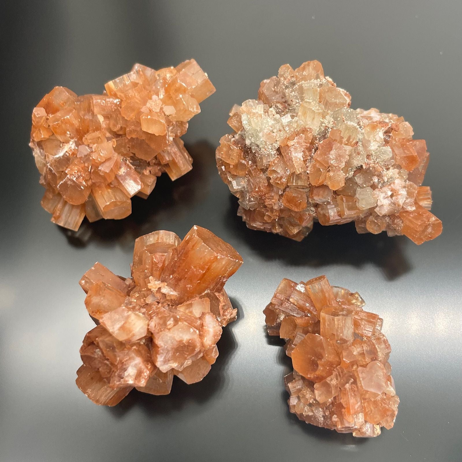Vier rohe, orangefarbene Aragonit-Kristallcluster auf schwarzem Hintergrund.