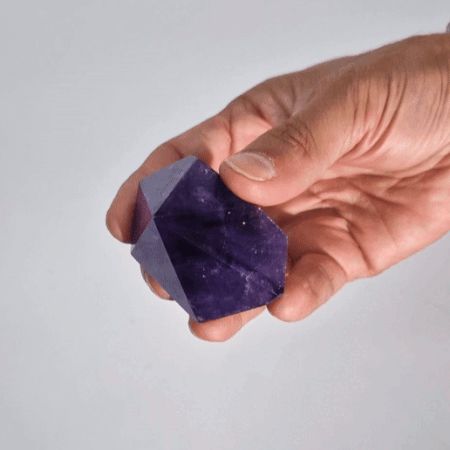 Eine Hand hält eine natürliche, facettierte Amethyst-Kristallspitze in intensivem Violett.