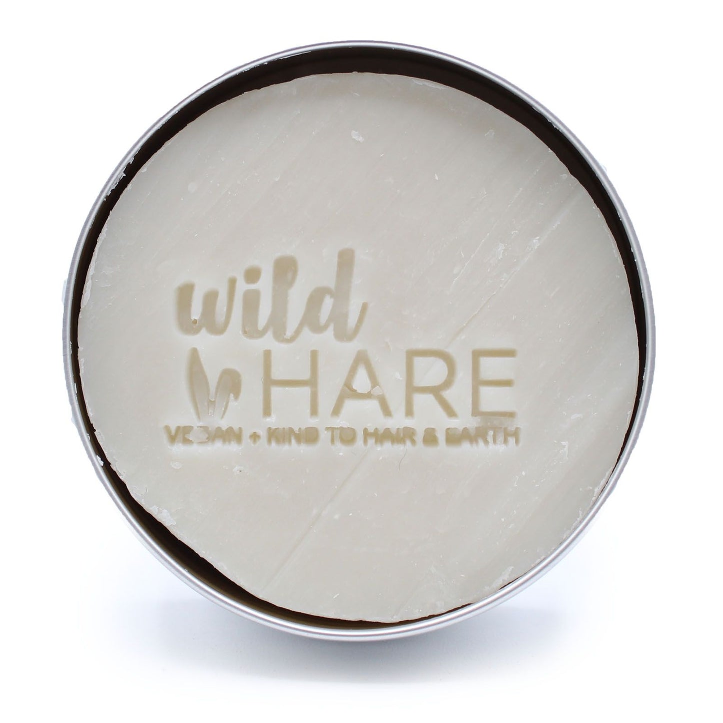 A round, white solid shampoo bar with "wild HARE" and "VEGAN + KIND TO HAIR & EARTH" embossed on it, in a silver tin.