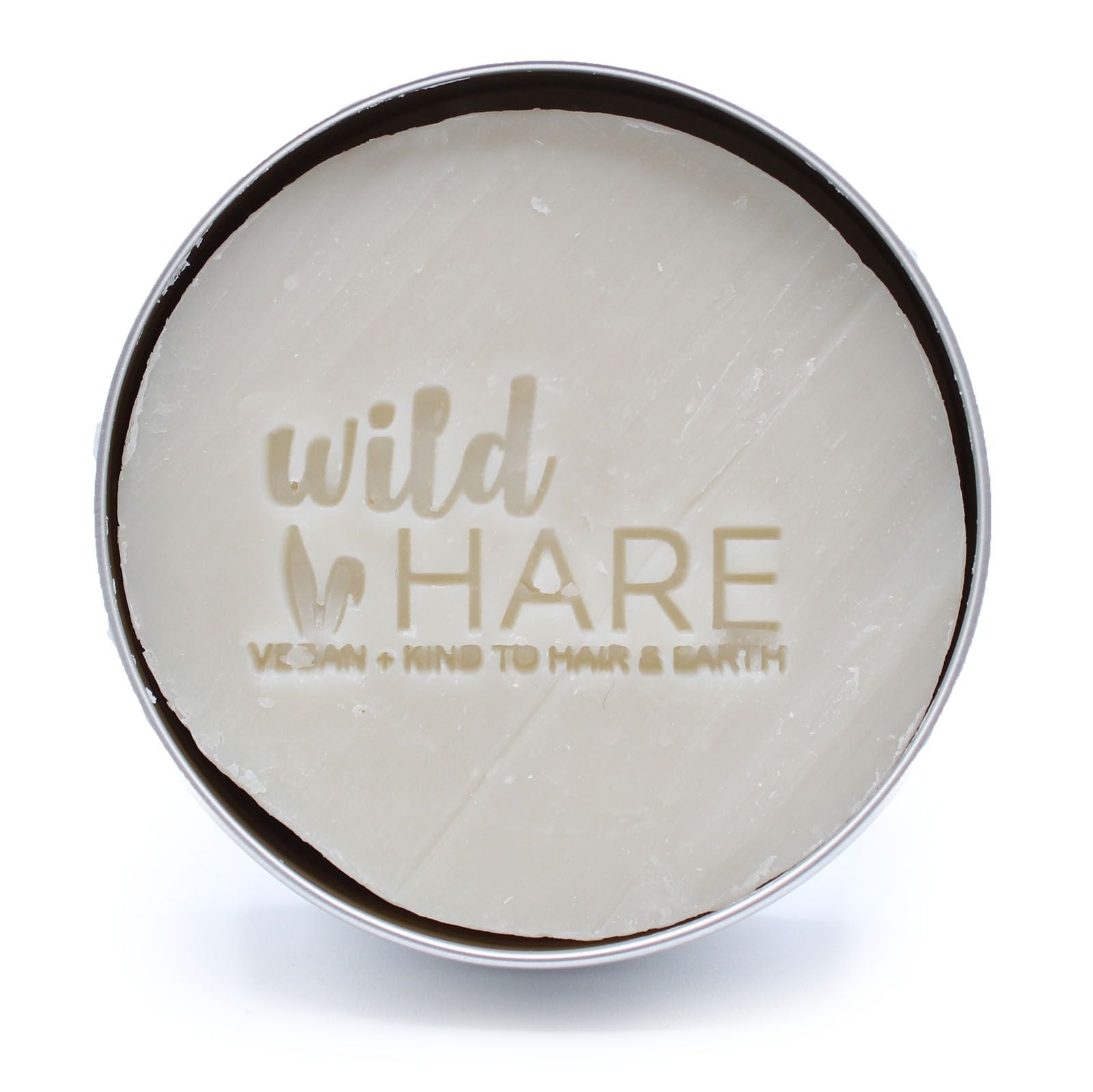 A round, white solid shampoo bar with "wild HARE" and "VEGAN + KIND TO HAIR & EARTH" embossed on it, in a silver tin.