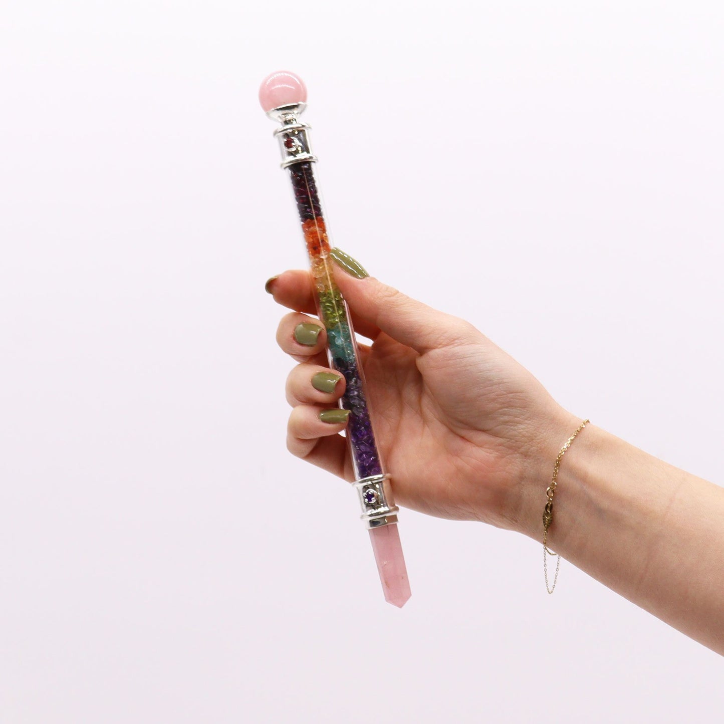 A hand holds a 7 chakra crystal healing wand with a rose quartz sphere and point.