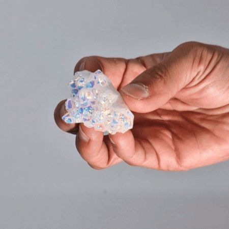 Hand hält einen natürlichen Angel Aura Cluster aus Quarz mit schillernden blauen und weißen Kristallen.