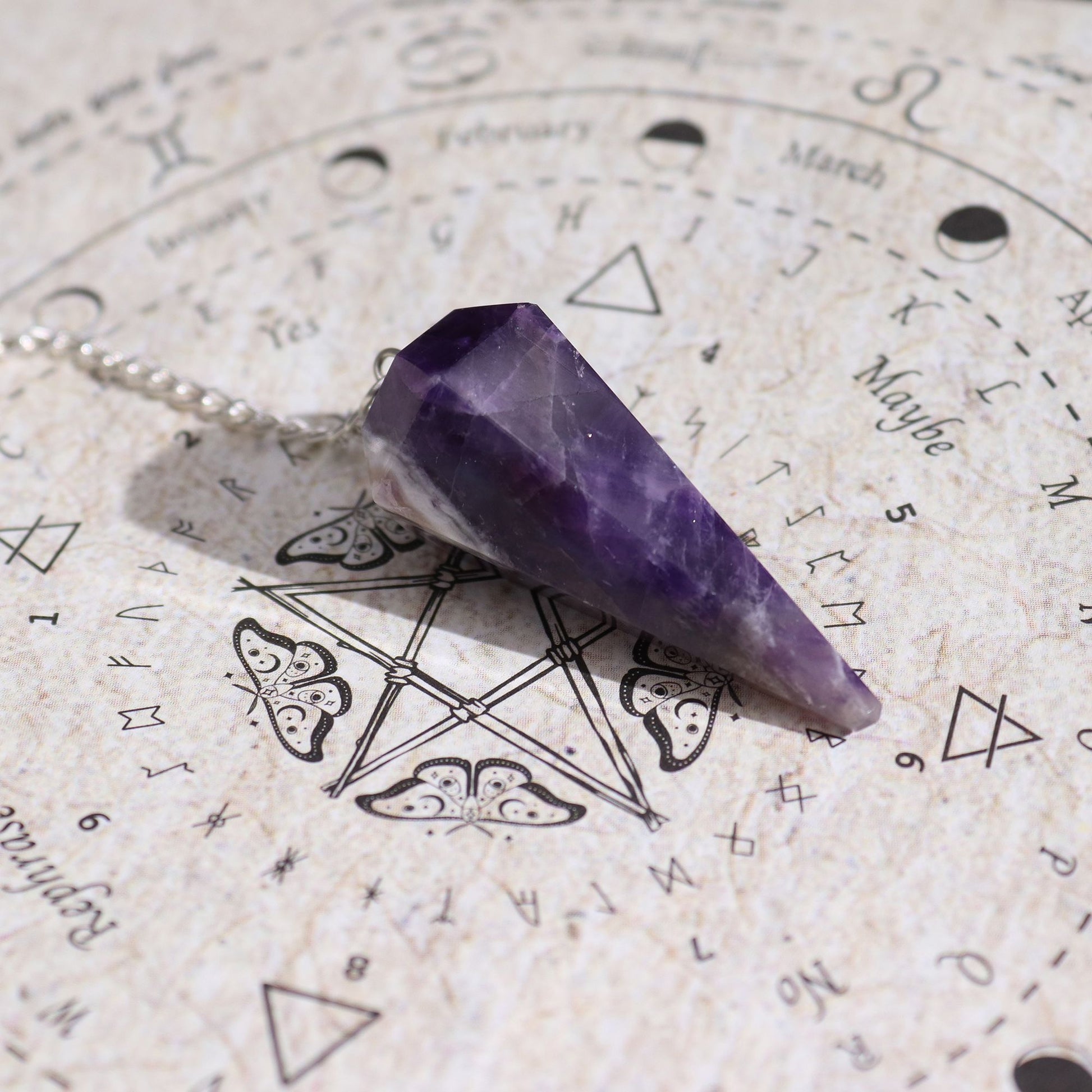Amethyst Pendel mit Kette auf einer Pendeltafel mit Symbolen.